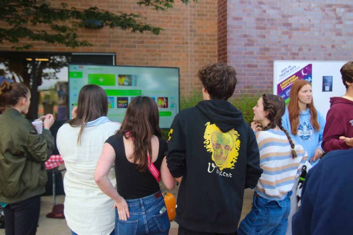 A group of friends try to decide which song they should choose at the Just Dance booth.