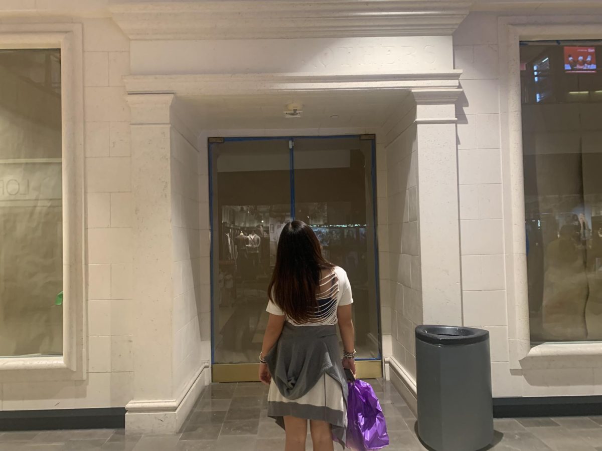 High schooler at the mall with a shopping bag in hand look up at an empty storefront
