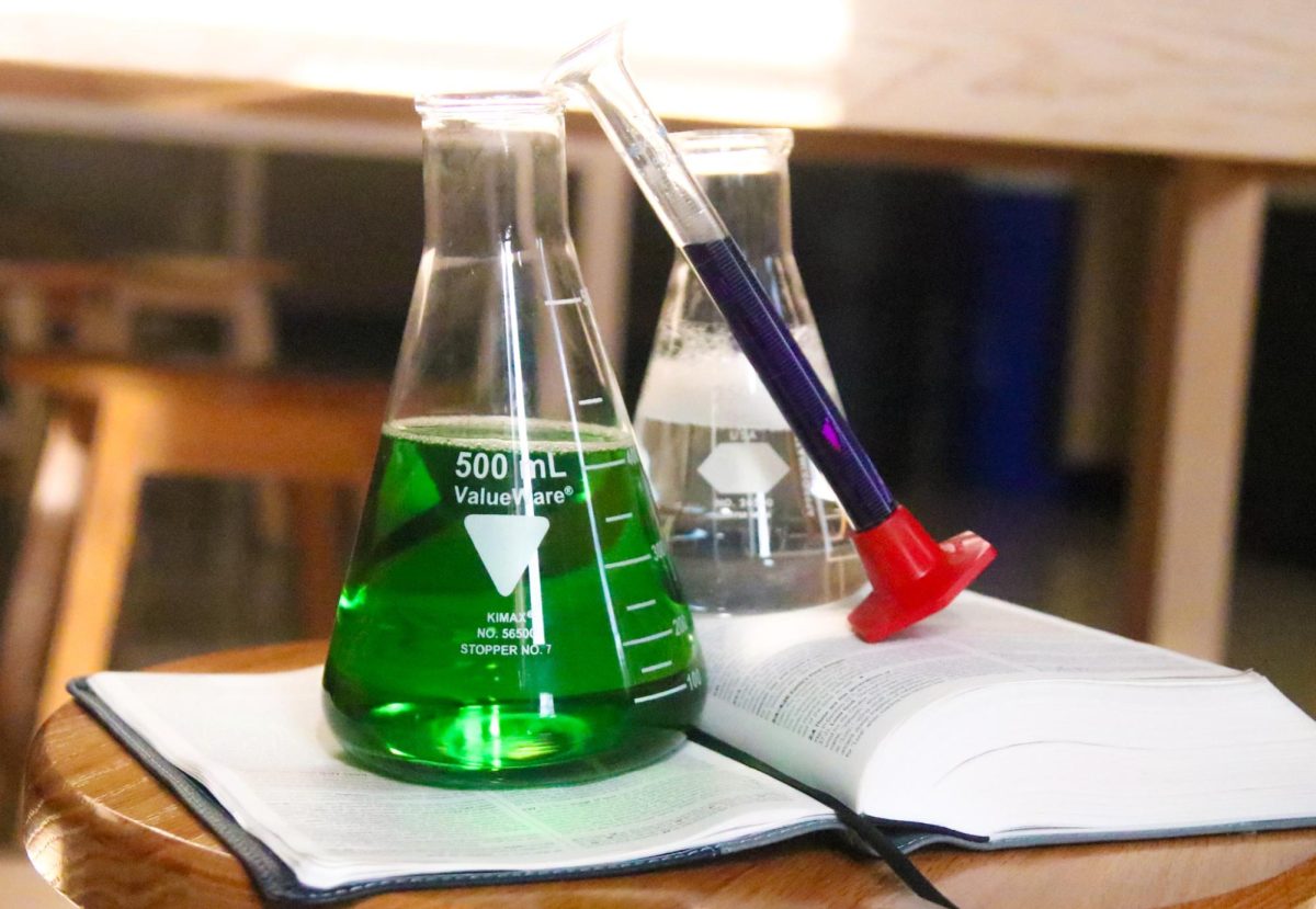 Two Erlenmeyer flasks and a graduated cylinder on top of a Bible flipped to Genesis 1 and 2