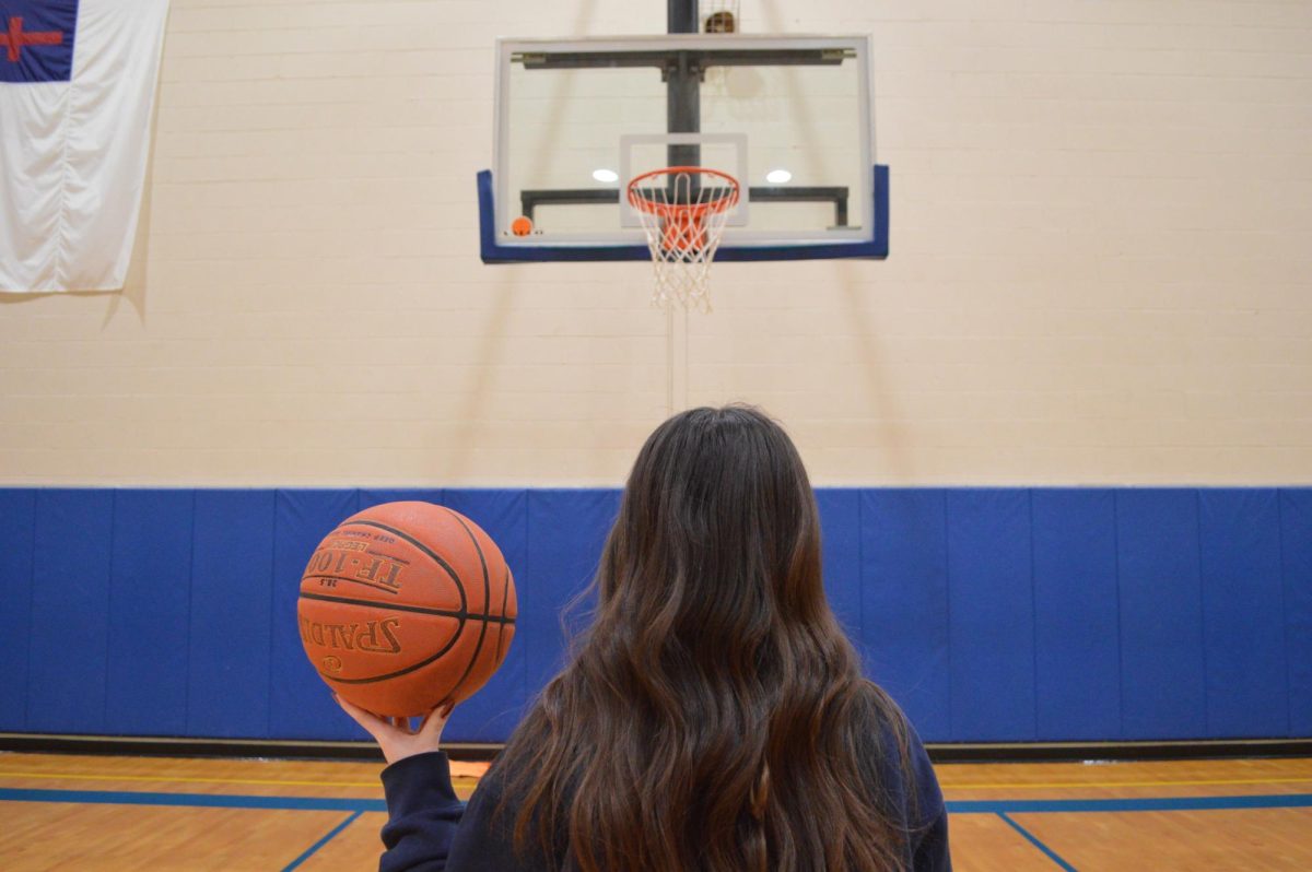 Female Westminster student holding a basketball looks up at a basketball hoop