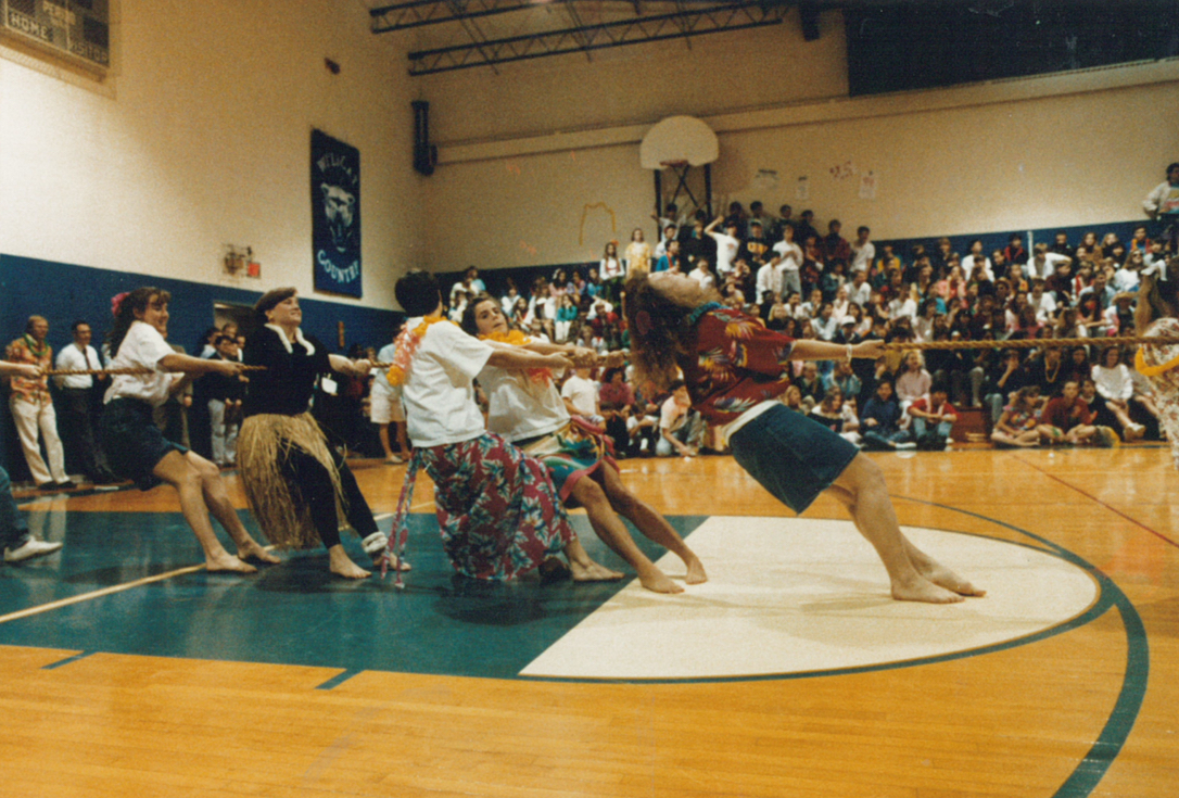 A girls’ tug-of-war match takes place with students cheering from the bleachers (1990)